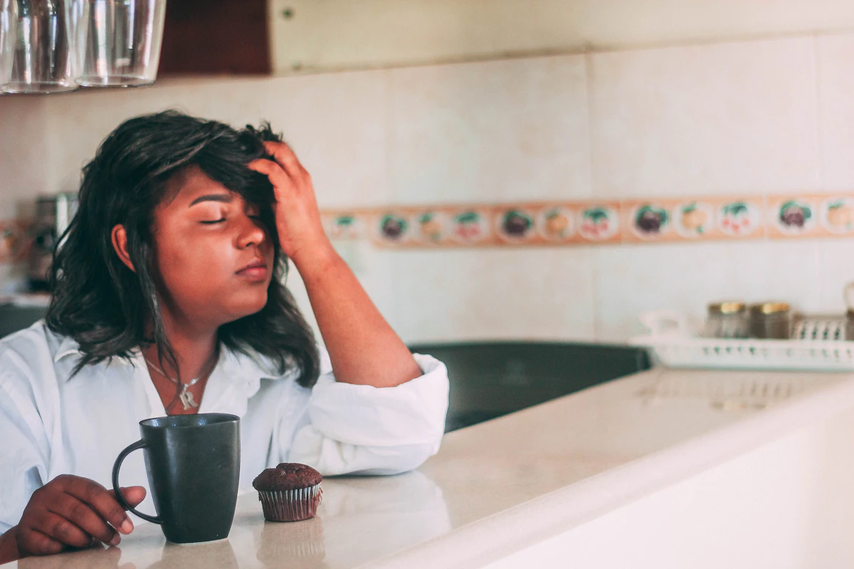 Mujer cansada apoyada en la encimera de la cocina junto a una taza