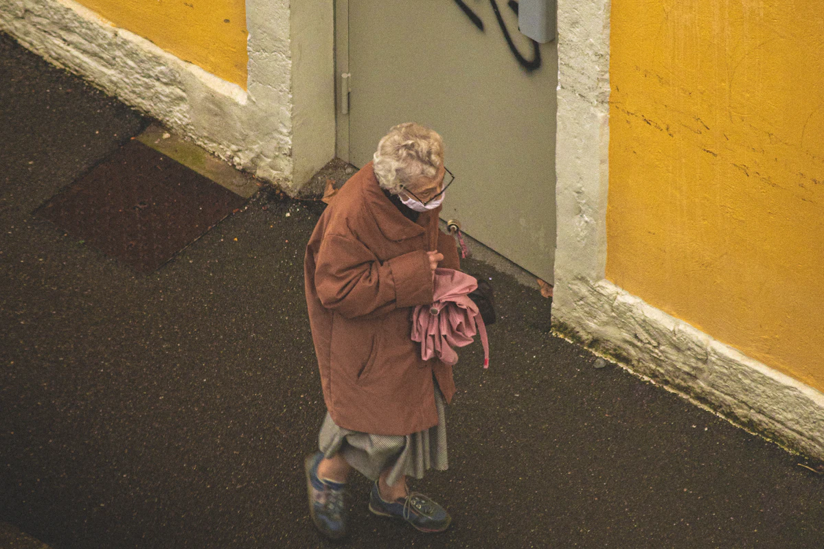 Señora mayor paseando por una calle junto a una pared amarilla