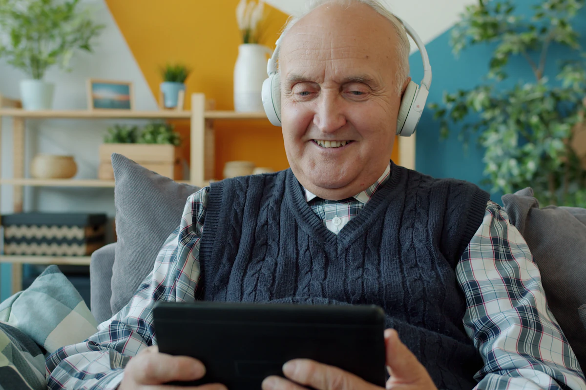 Señor mayor sonriendo con una tablet y auriculares en su salón